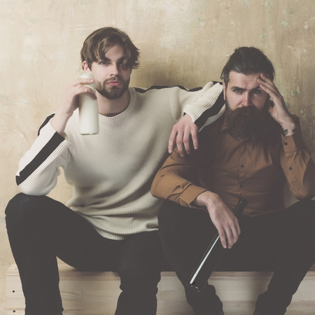 two young handsome men friends drinking wine and yogurt while resting on beige backgroundの写真素材