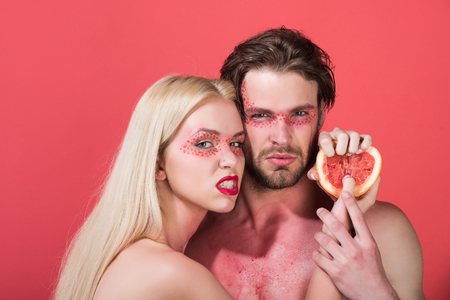 couple with grapefruit. woman and man with creative fashionable makeup on face hold fruit on red background, beauty and fashion, allergy, healthcare and vitamin, vegetarian and dietingの写真素材