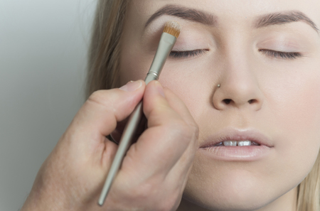 Girl getting eyeshadow powder on eyelids with brush. Eye makeup for pretty woman with young healthy face skin on grey background. Visage, skincare, cosmetics, make upの写真素材