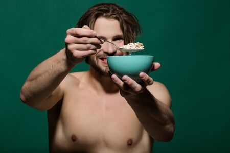 bowl with porridge or cereal of oatmeal wih milk in hand of naked muscular happy man on green backgroundの写真素材