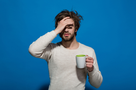 morning. sleepy tired man with headache hold cup of tea or coffee has uncombed hair in underwear on blue background, morning refreshment and drinkの写真素材
