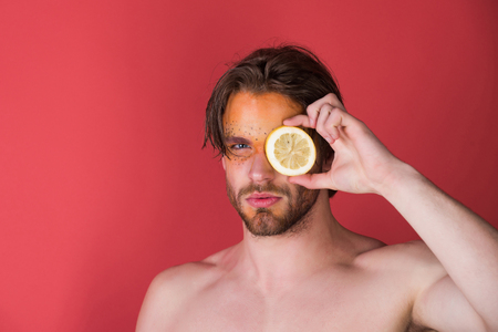 handsome man with creative fashionable makeup on face hold lemon fruit in hand on red background, beauty and fashion, allergy, healthcare and vitamin, vegetarian and dieting, copy spaceの写真素材