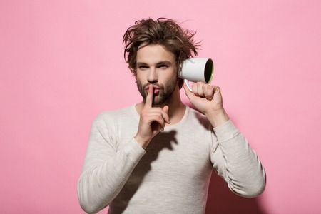 hush gesture of man overhear with cup in morning on pink backgroundの写真素材