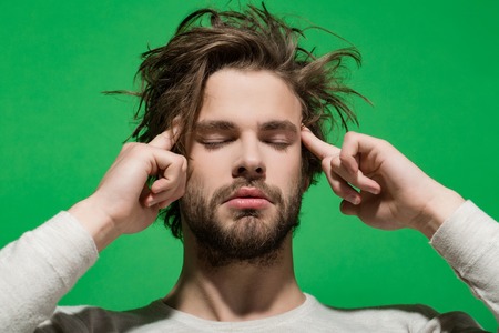 headache. tired guy or handsome man with beard and stylish hair in white underwear on green background, morning and fashionの写真素材