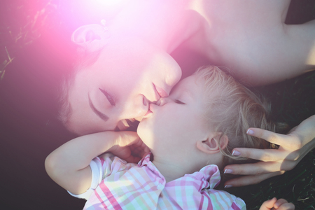 Smiling cute baby boy, small, little, son, and pretty mother, woman, lying on green grass on sunny summer nature outdoors on natural background. Happy mothers day, family loveの写真素材