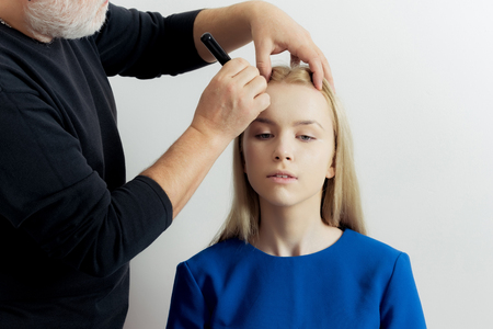 Girl or woman getting makeup on face skin with powder brush by male visagiste. Adorable fashionable model with long blond hair in beauty salon. Visage, cosmetics, make up. Beauty, youthの写真素材