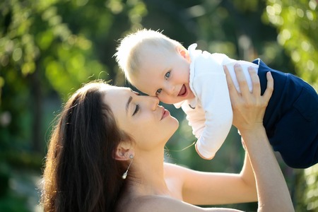 Happy cute baby boy, small, little, son, and pretty mother, woman, with long hair having fun, smiling, on sunny summer nature outdoors on natural background. Mothers day, family loveの写真素材