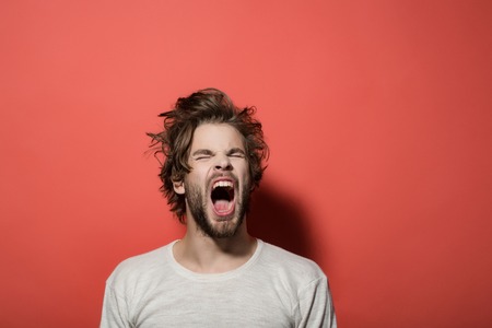 shouting or yawning man with disheveled and uncombed long hair with beard in white underwear on red background, morning and wake up, everyday life, headacheの写真素材