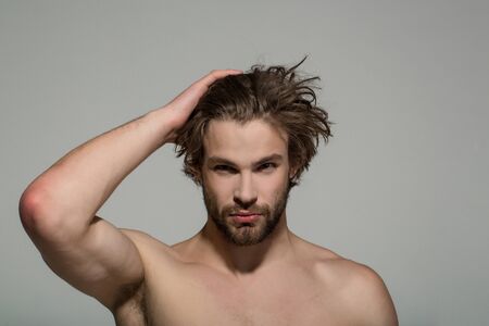 handsome man with beard and stylish hair with raised hand and bare chest on grey background, morning and fashionの写真素材