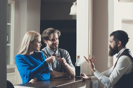 Woman and man toasting glasses of wine at bar. Girl and macho talking to bartender with bottle at counter. Couple in love. Date and dating. Alcohol, appetizer and aperitif. Addictive and conviveの写真素材