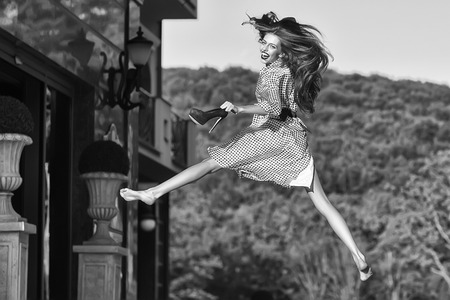 woman or girl with long hair in black and white blouse holding high heeled shoes and jumping, retro old vintage black and white styleの写真素材