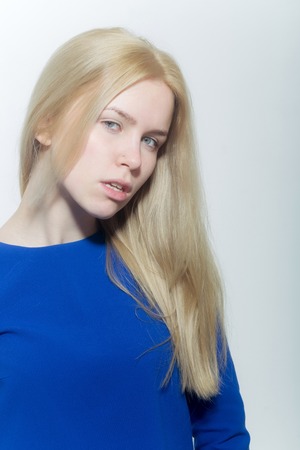 Girl with blond long hair and no makeup on pretty face. Sexy woman posing in blue dress on white background. Cosmetics and skincare. Cosmetology. Beauty and hairdressing salonの写真素材