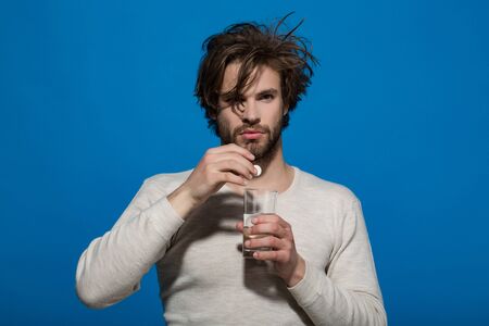 Drug and antidepressant. Guy hold dieting pill or vitamin and water glass. Health and medicine. Treatment and hypnotic tablet. Man drink pill with water from glass.の写真素材