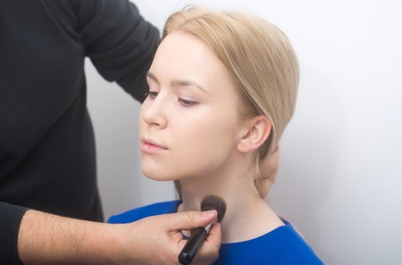 Male hands with makeup brush applying powder on girl neck skin. Adorable woman with young cute face and natural make up on white background. Visage, cosmetics and skincare. Beauty salonの写真素材