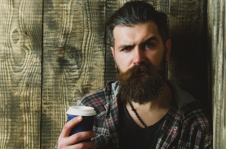 hipster. Frown man with grey hair, long beard and moustache holding blue plastic cup on wooden background. Coffee to go. Healthy lifestyle and dietingの写真素材