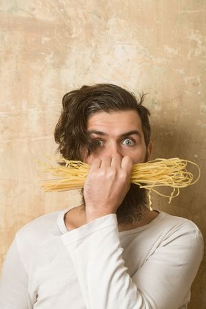 Man with pasta in hand. Hipster hold Italian macaroni. Healthy food and dieting. Cook or chef bearded man. Cooking raw spaghetti in restaurant.の写真素材