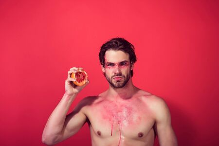 handsome man with creative fashionable makeup on face hold grapefruit fruit in hand on red background, beauty and fashion, allergy, healthcare and vitamin, vegetarian and dietingの写真素材