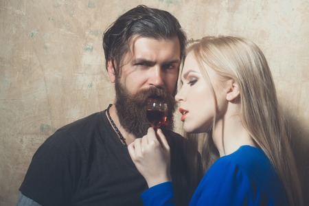 Hipster and woman relaxing with glass of red liqueur. Cute girl with blond long hair and brutal man on beige background. Couple in love. Alcohol and appetizer. Unhealthy lifestyle and bad habitsの写真素材