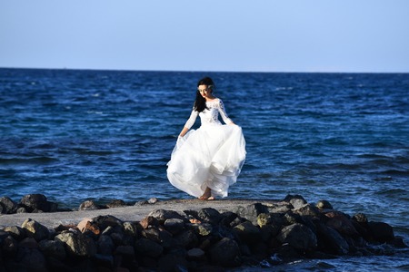 Bride beautiful woman alone in elegant white dress walking along beach and blue sea outdoorの写真素材