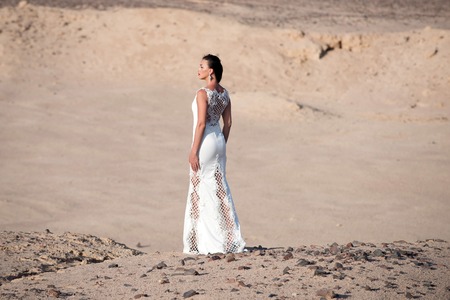 Bride young pretty woman brunette posing back in beautiful long white wedding bridal dress on background of sand desertの写真素材