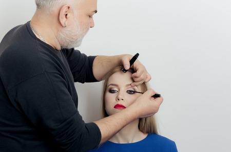 Makeup artist applying black mascara on girl eyelashes with make up brush. Woman, pretty fashion...