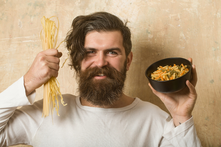 Cooking raw spaghetti in restaurant. Healthy food and dieting. Man smiling with pasta in hand. Cook or chef bearded man with bowl. Hipster hold Italian macaroni.の写真素材