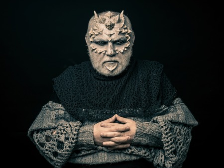 Demon with folded hands isolated on black. Alien or reptilian makeup with sharp thorns and warts....