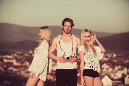 Girl and women with photographer outdoor. Guy with photo camera on athletic chest. Love and romance. Beauty and art fashion. Man with muscular body with twins.の写真素材