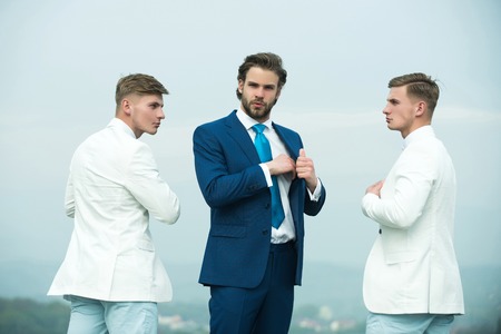 Men posing on blue sky. Boss and employees on sunny day. Group of business people wearing formal...