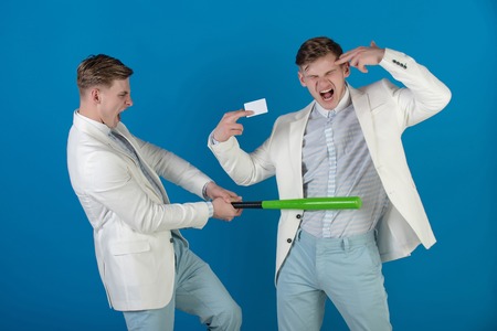 Managers shouting and fighting on blue background. Man showing finger gun with blank card. Businessman batting rival with baseball bat. By force or persuasion. Business negotiations concept.の写真素材