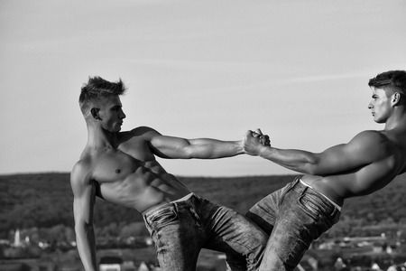 men or bodybuilders, athletes with sexy, muscular torsos with six packs, abs, biceps, triceps wrestling outdoor in mountains on sky, black and whiteの写真素材