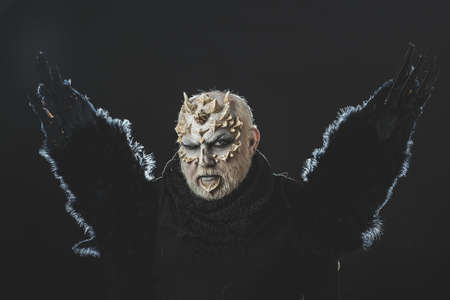 Dragon with white eyes and beard on face. Man with black bird wings on dark background. Wizard with thorns and horns on skin. Demon with raven or crow feathers. Magic and mystery concept.の写真素材