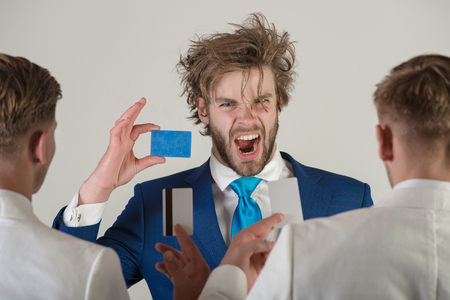 Man shouting with angry face and blue card in hand facing two businessmen, back view, on grey background. Business ethics concept.の写真素材