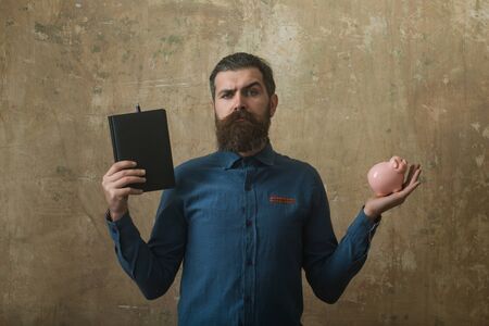 man or businessman with serious face hold notebook and money box on beige backgroundの写真素材