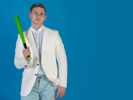 Businessman wearing white jacket, shirt and pants. Fashion and sport. Baseball player posing on blue background. Power and energy concept. Man holding green bat, copy spaceの写真素材