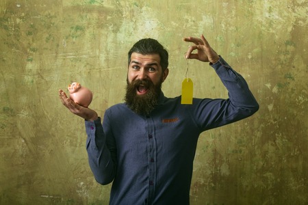 Guy hold shopping tag and moneybox. Loan and bankruptcy. Businessman take bank credit. Money and success. Man with beard on happy face.の写真素材