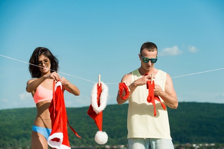 Christmas man and woman family. New year guy with muscular body on blue sky. Couple of happy man and girl hanging clothes for drying. Laundry and dry cleaning. Xmas red costume on rope with pin.の写真素材