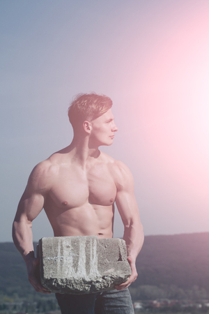 Man builder with muscular body. Athletic bodybuilder as hercules. Gladiator or atlant. Sport and workout. Adam hold bog stone.の写真素材