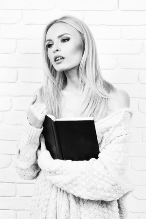 girl or beautiful cute woman fashion model with blond hair in sexy knitted sweater reads book on brick wall, black and whiteの写真素材