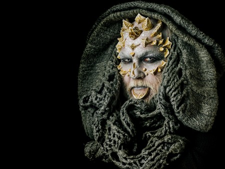 Monster face with white eyes, thorns and warts. Alien or sorcerer makeup. Demon head with grey hood isolated on black. Horror and fantasy concept. Man with dragon skin and beard, copy spaceの写真素材