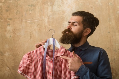Man with beard hold dress and tape measure in workshop on beige backgroundの写真素材