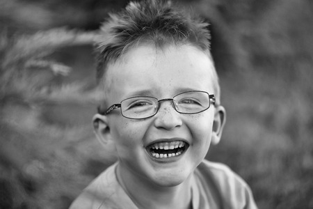 Happy baby boy with hair in shirt and eyeglasses on happy smiling face summer day outdoor on natural background, black and whiteの写真素材