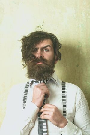 Hipster in shirt and suspenders with musical tie. Man with long beard and mustache on serious face....