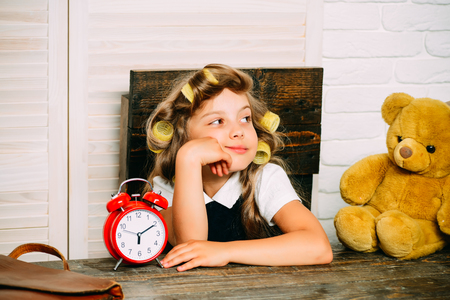 Small girl with curler in hair. Little baby secretary with bear. Kid choose career. Child with alarm clock. Education and childhood.の写真素材