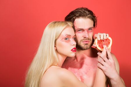grapefruit at girl and man with creative fashionable makeup on face hold grapefruit fruit on red background, beauty and fashion, allergy, healthcare and vitamin, vegetarian and dieting, couple in loveの写真素材