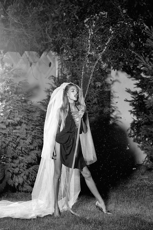 girl bride in dress and veil holding hose with water drops outdoor in evening, black and whiteの写真素材