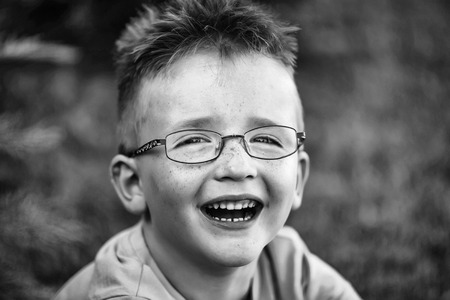 Happy baby boy with hair in shirt and eyeglasses on happy smiling face summer day outdoor on natural background, black and whiteの写真素材