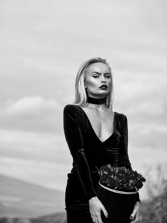 woman or beautiful blond woman in sexy dress with rose flowers in box outdoor on natural background with cloudy sky, black and whiteの写真素材