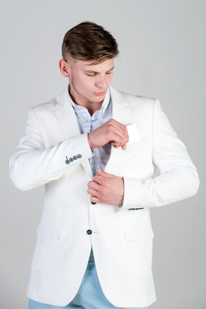 Boss putting business or bank card in pocket. Man wearing white jacket, striped shirt and blue pants. Model posing in casual suit on grey background. Fashion and information conceptの写真素材