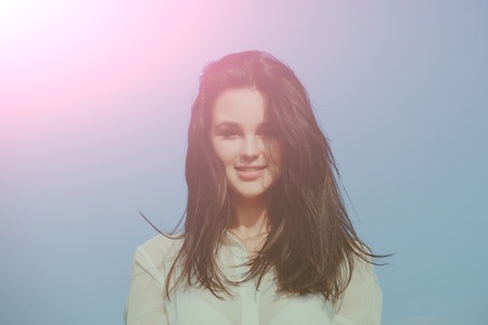 woman with happy face and long brunette hair sunny outdoor on blue backgroundの写真素材